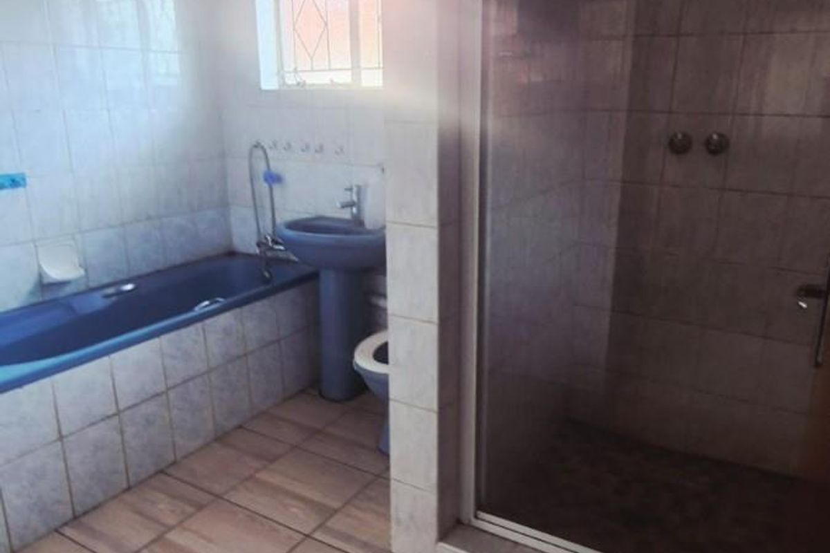 A dated bathroom featuring a blue bathtub and pedestal sink, a separate glass-enclosed shower, and tiled flooring throughout.