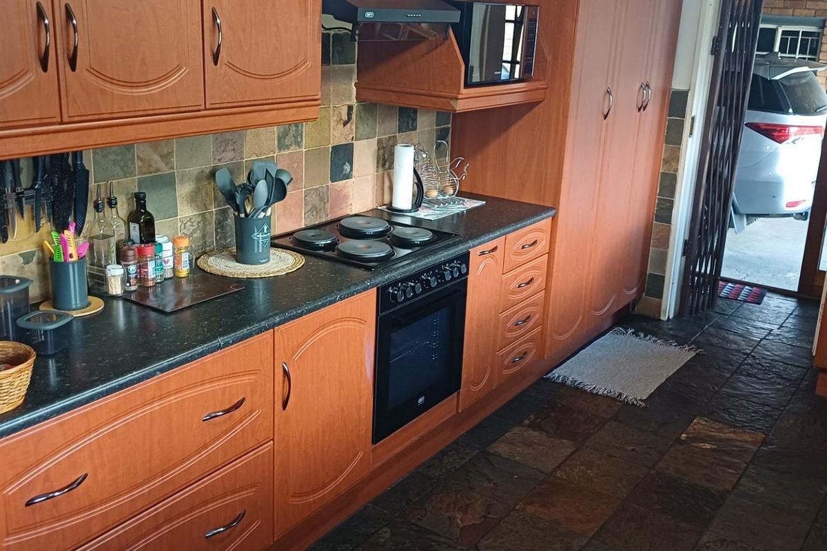 A functional kitchen featuring wood-finish cabinetry, stone-look tile flooring, a built-in oven, and a hob with an extractor fan.