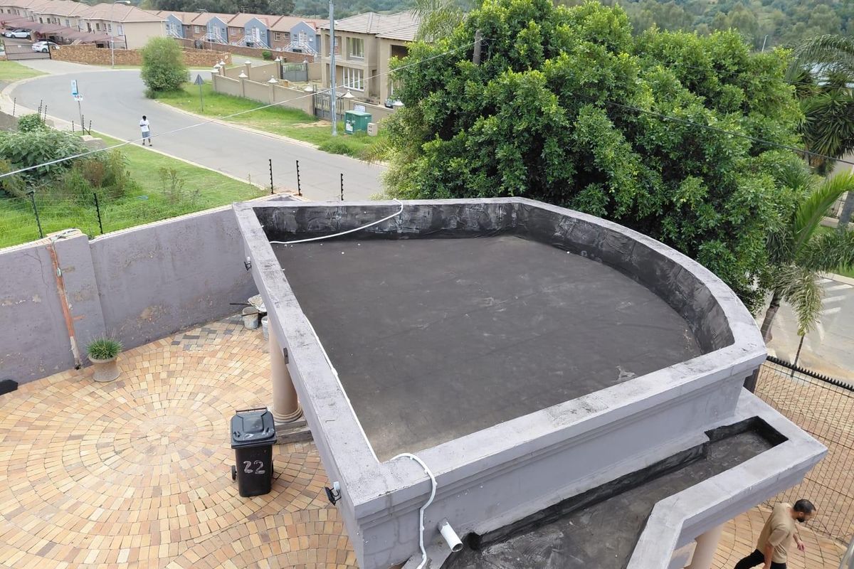 Elevated view of a flat roof structure with visible waterproofing membrane, adjacent to a paved courtyard area in a residential estate setting.
