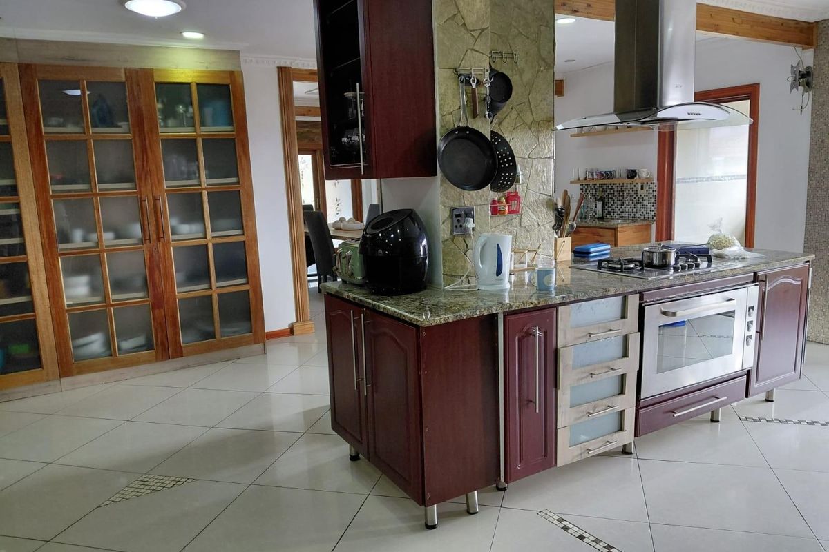 Spacious kitchen featuring a central island with built-in gas hob, stainless steel extractor fan, oven, and extensive wooden cabinetry with glass-fronted display units.