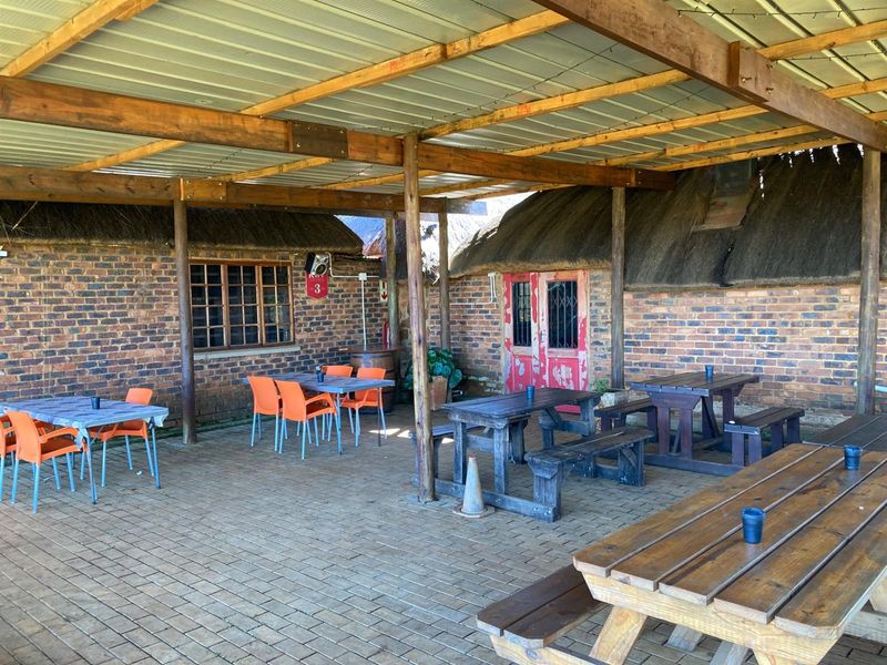 A covered outdoor patio area featuring rustic brick walls, thatched roof sections, and paved flooring, suitable for social gatherings or entertainment.