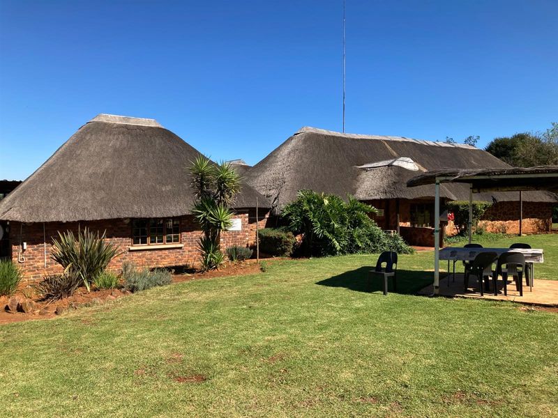 Rear view of a traditional brick-built small holding featuring classic thatched roofing, a covered patio area, and established garden surroundings.