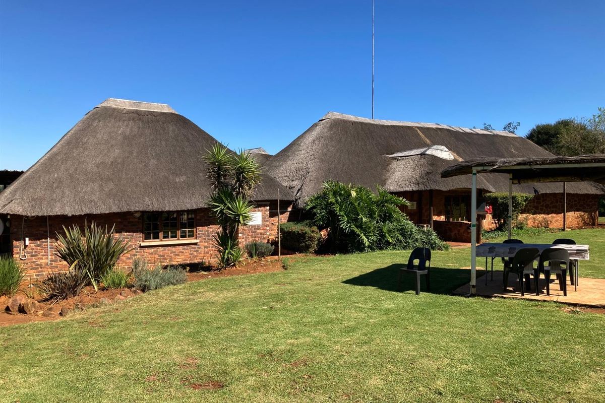 Rear view of a traditional brick-built small holding featuring classic thatched roofing, a covered patio area, and established garden surroundings.