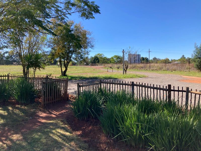A view of the property grounds featuring a gravel driveway, established trees, and a rustic wooden perimeter fence.