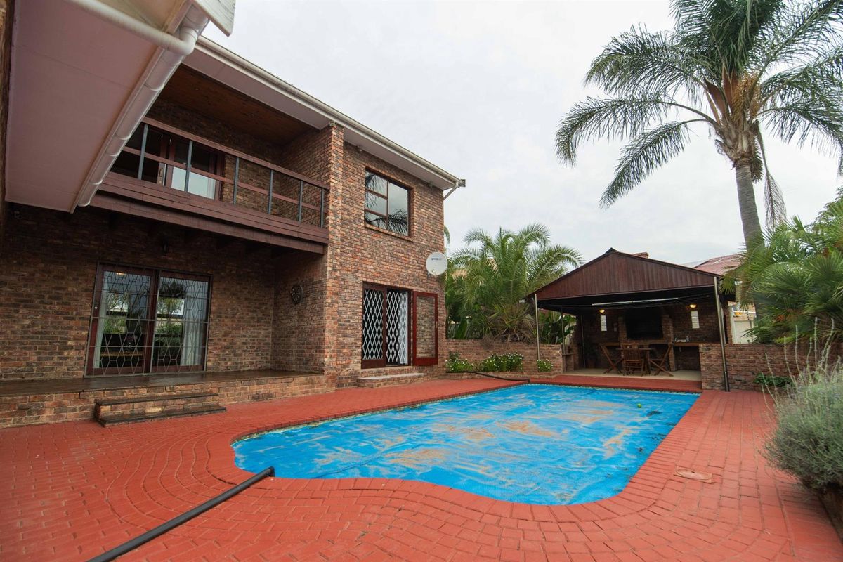 Rear exterior view featuring a brick facade, swimming pool with cover, and a covered outdoor entertainment area with built-in braai.