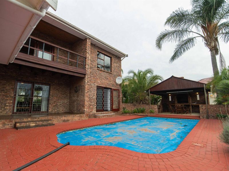 Rear exterior view featuring a brick facade, swimming pool with cover, and a covered outdoor entertainment area with built-in braai.