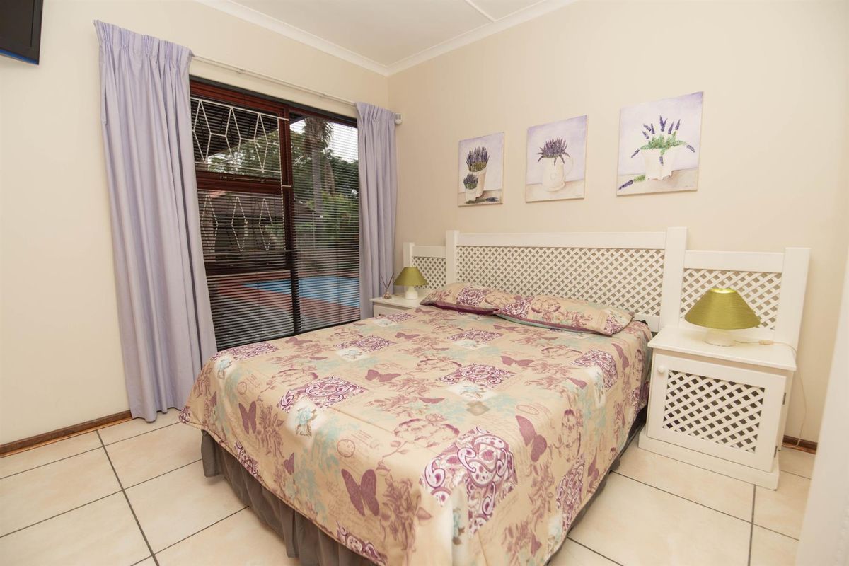 A bedroom featuring tiled flooring, a built-in lattice headboard, and sliding glass doors providing direct access to the outdoor pool area.