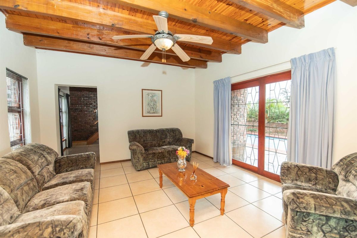 A living room featuring exposed timber ceiling beams, tiled flooring, and sliding glass doors providing direct access to the outdoor pool area.