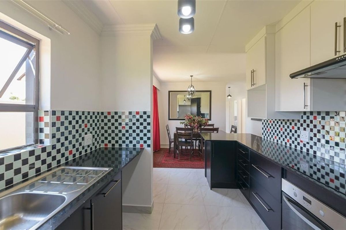 Modern kitchen featuring dark cabinetry, granite countertops, and a distinctive checkered mosaic tile backsplash, flowing into an adjacent dining area.