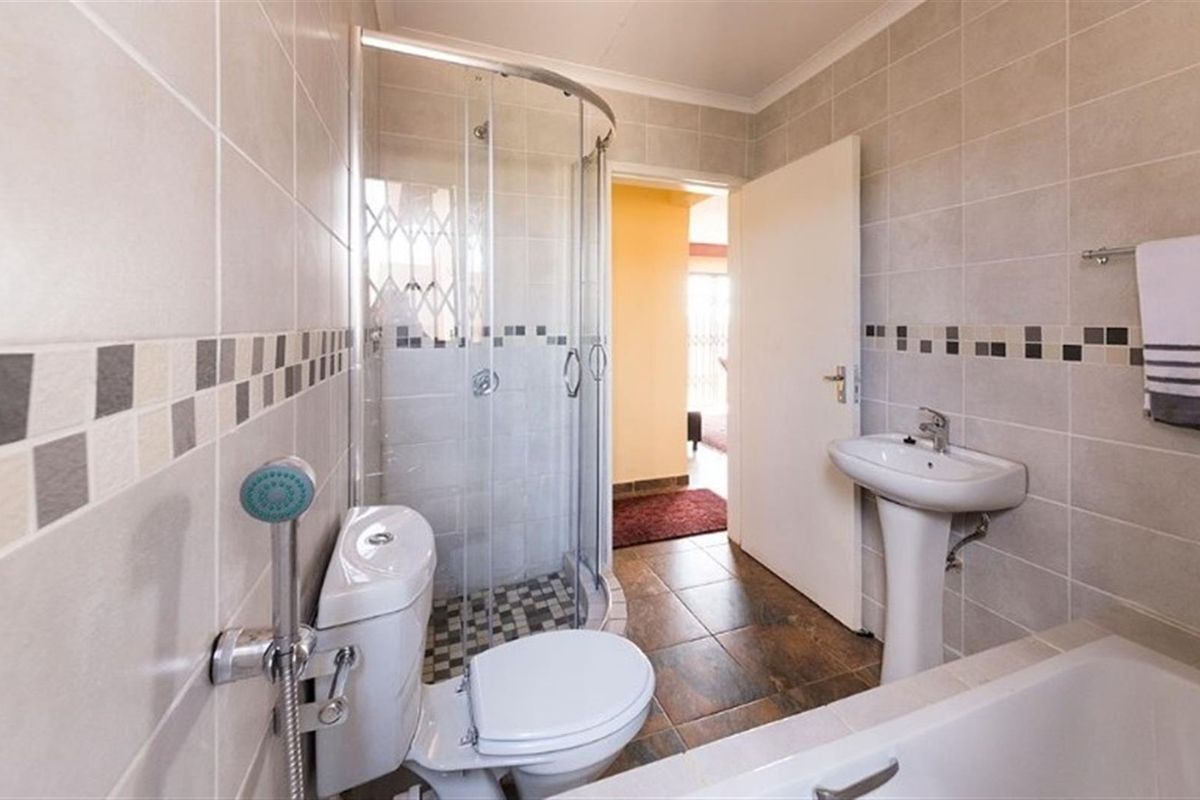 A functional bathroom featuring a corner shower enclosure, pedestal basin, and bathtub with neutral wall tiling and tiled flooring.