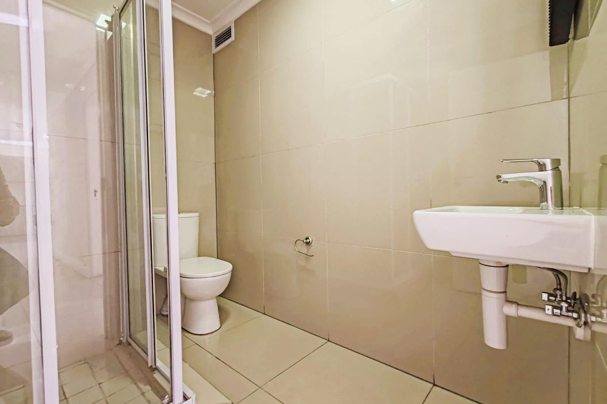 A modern bathroom featuring a glass-enclosed shower, wall-mounted basin with chrome faucet, and a standard toilet, finished with neutral floor-to-ceiling wall tiles.