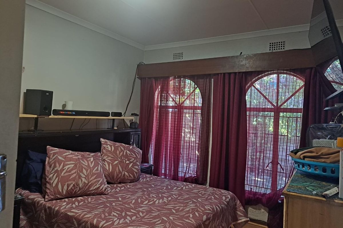 A bedroom featuring distinctive arched windows with security bars and a timber pelmet, providing a functional space with natural light.