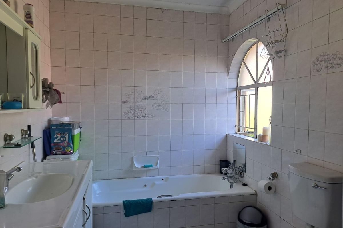 A dated bathroom featuring a built-in bathtub, vanity basin, and toilet, finished with full-height wall tiling and an arched window.