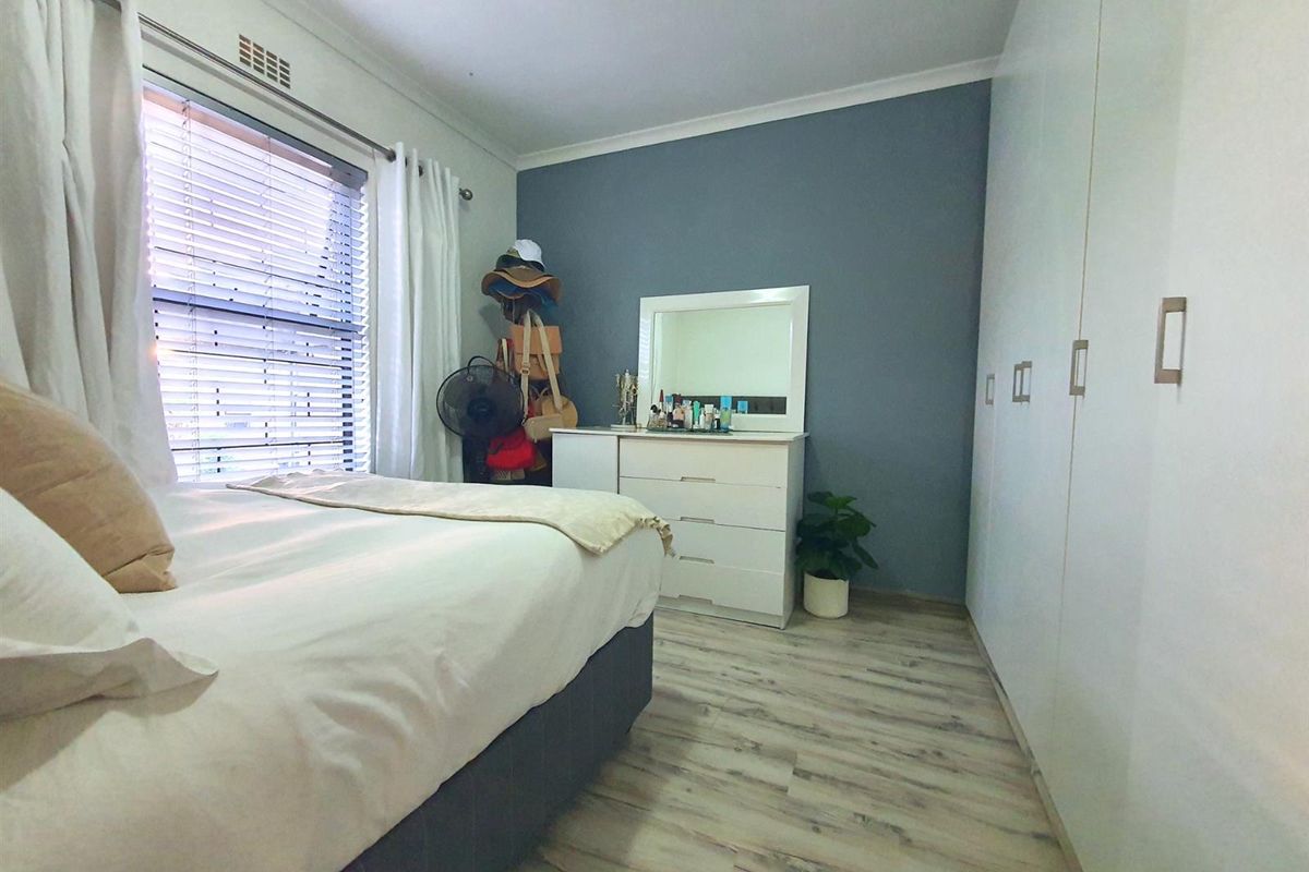 A well-maintained bedroom featuring built-in cupboards, laminate flooring, and a feature wall, offering a clean and functional living space.