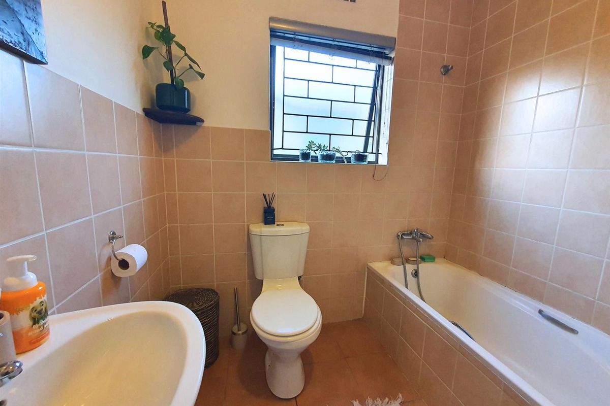 A functional bathroom featuring a bathtub, pedestal basin, and toilet, finished with neutral ceramic wall and floor tiles.