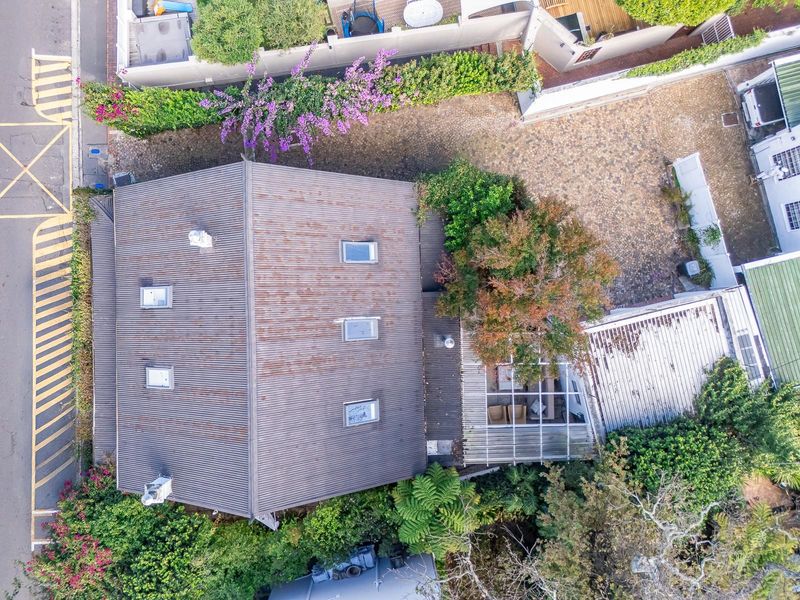 Aerial view of the property showing a metal roof with visible signs of corrosion and wear, surrounded by established garden landscaping.