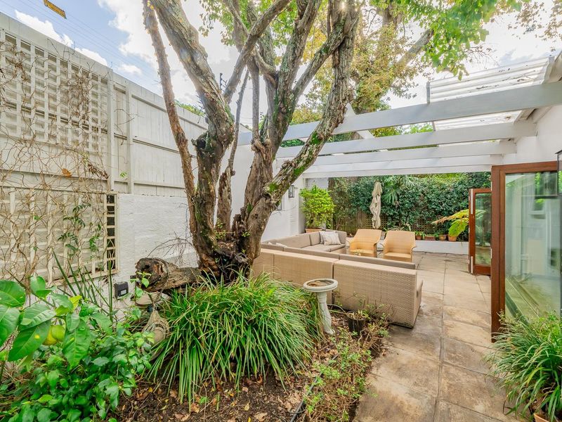 A private outdoor patio area featuring a timber pergola, paved flooring, and established garden elements, providing a tranquil space for relaxation.