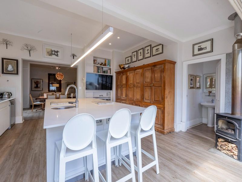 Open-plan kitchen featuring a central island with sink, modern cabinetry, and a freestanding wood-burning fireplace, seamlessly connecting to the dining area.