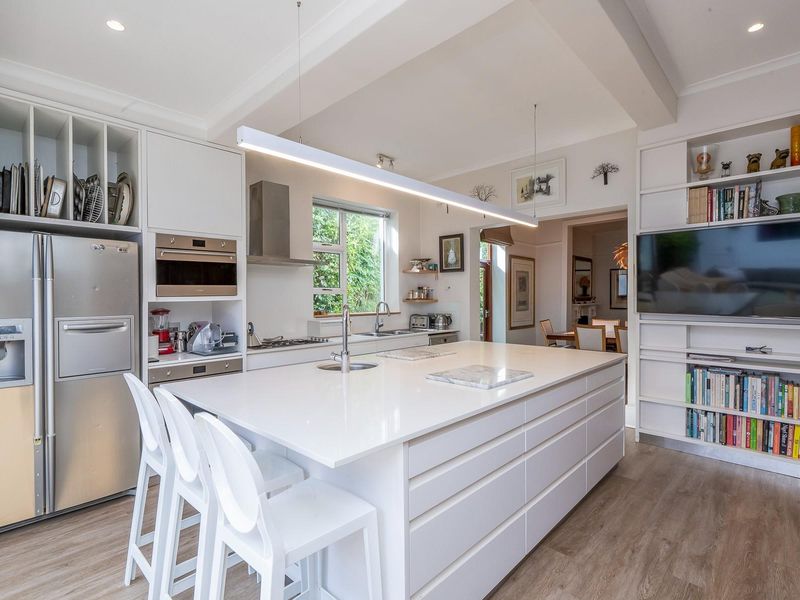 Modern open-plan kitchen featuring a large central island with stone countertops, integrated cabinetry, built-in appliances, and custom floor-to-ceiling shelving.