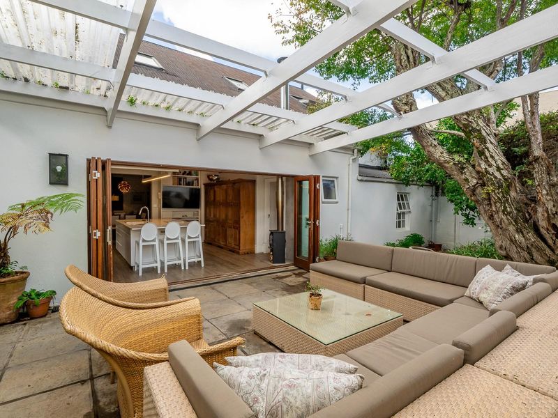 A covered patio area featuring a timber pergola, stone paving, and seamless flow into the open-plan kitchen and living space through folding doors.