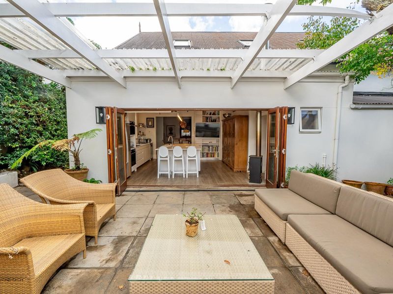 A covered outdoor patio area featuring a timber pergola, seamlessly connecting to an open-plan interior living and kitchen space through folding glass doors.