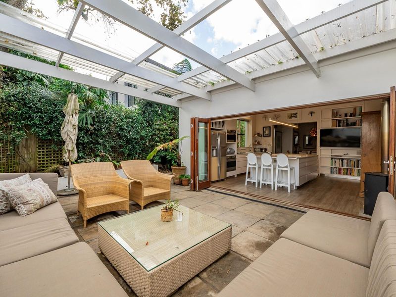 An indoor-outdoor living space featuring a covered patio with stone paving, seamlessly connecting to a modern kitchen through folding glass doors.