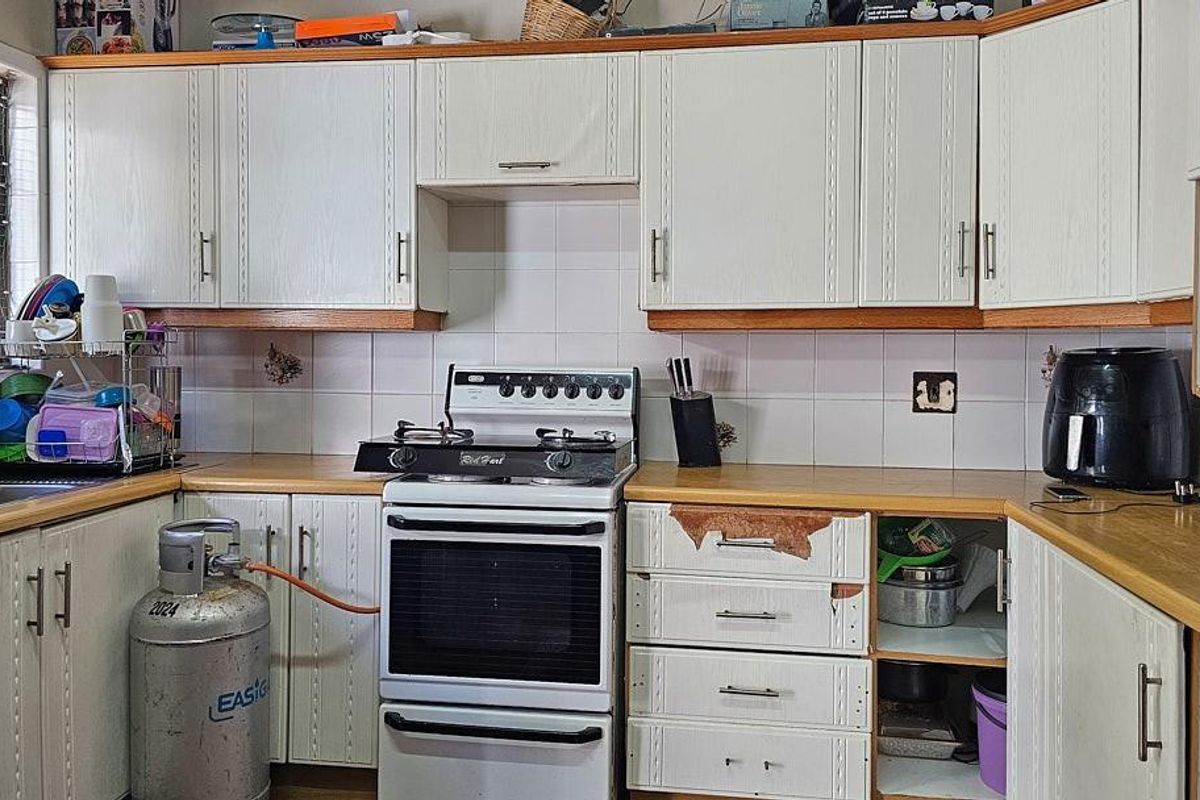 A functional kitchen featuring white cabinetry, a gas stove, and tiled splashbacks, requiring some cosmetic updates to the cabinetry and finishes.