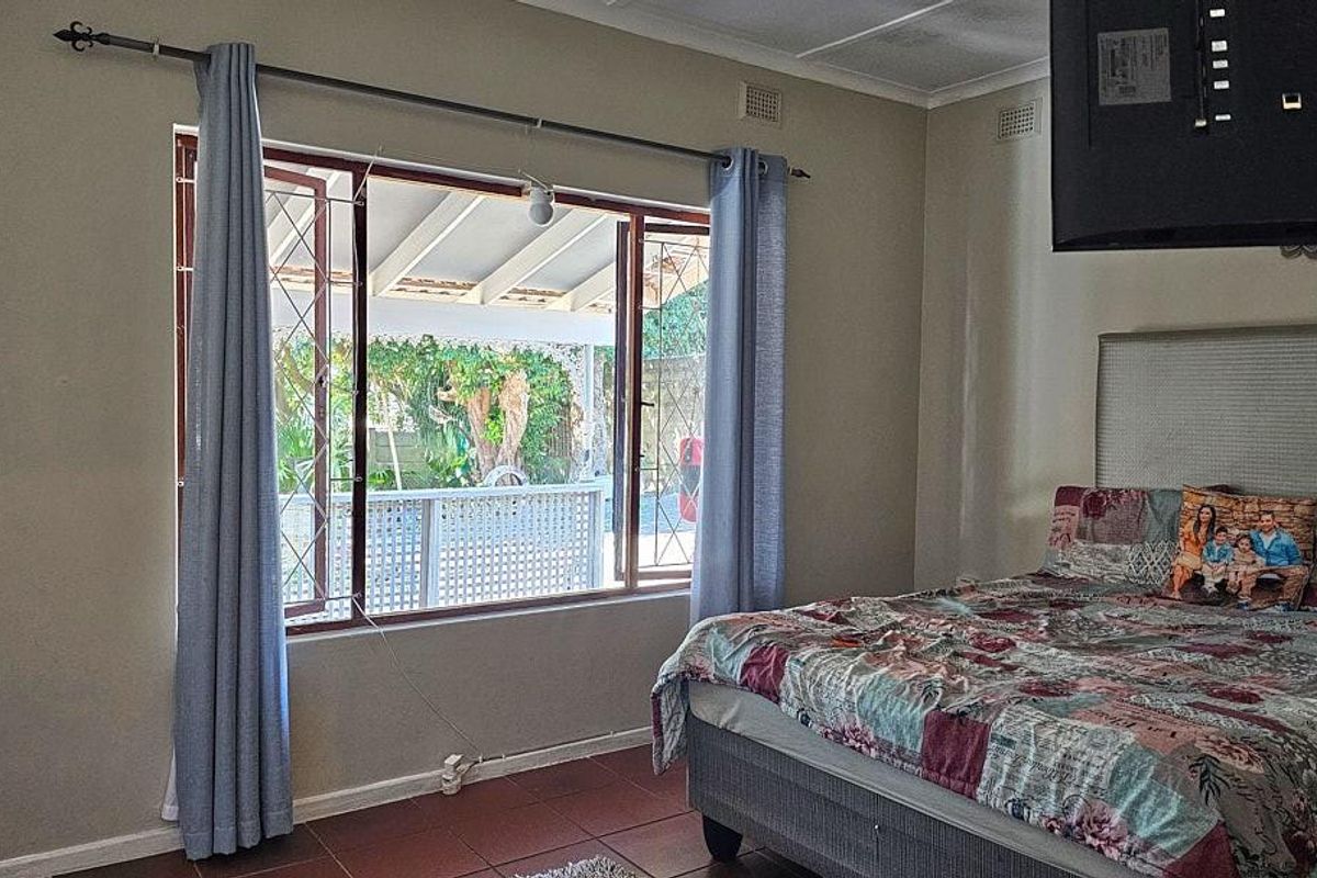 A bedroom featuring tiled flooring, a large window with security bars, and a view overlooking the outdoor patio area.