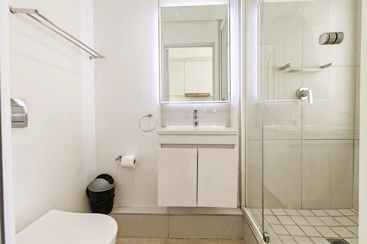 Modern bathroom featuring a glass-enclosed shower, wall-mounted vanity with integrated basin, illuminated mirror, and contemporary toilet.
