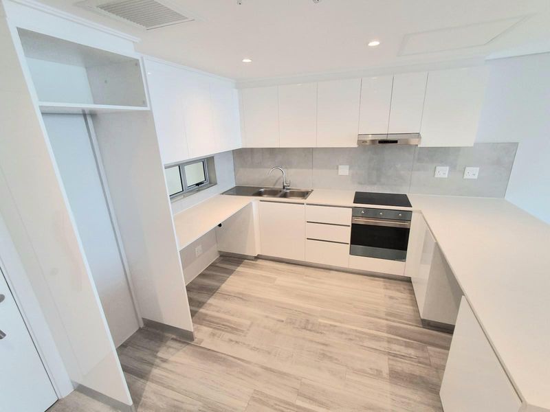 Modern kitchen featuring white cabinetry, stone countertops, integrated electric oven and hob, stainless steel sink, and light wood-look flooring.