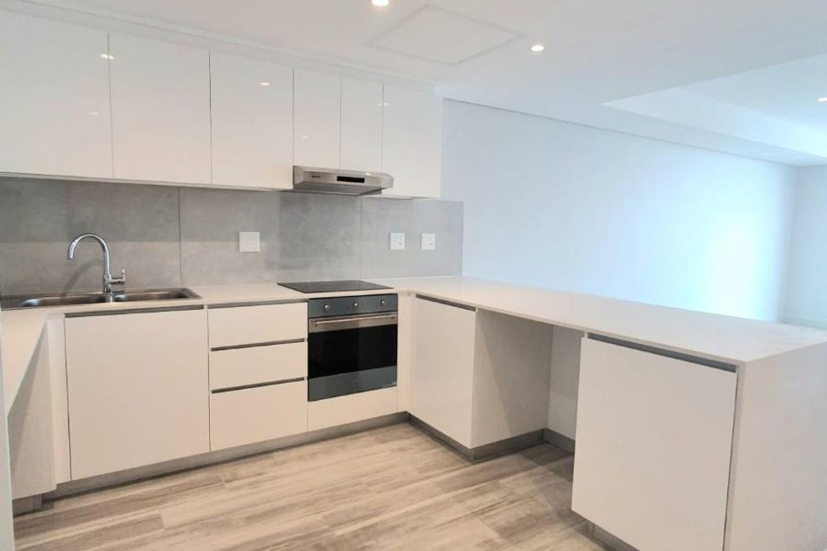 Modern kitchen featuring sleek white cabinetry, stone countertops, integrated oven, hob, extractor fan, and durable wood-look flooring in an open-plan layout.