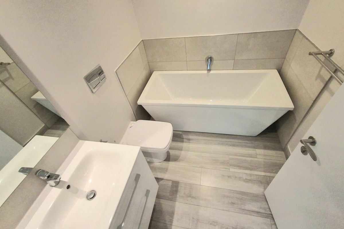 Modern bathroom featuring a sleek freestanding bathtub, wall-mounted toilet with concealed cistern, and a contemporary vanity unit with integrated basin.