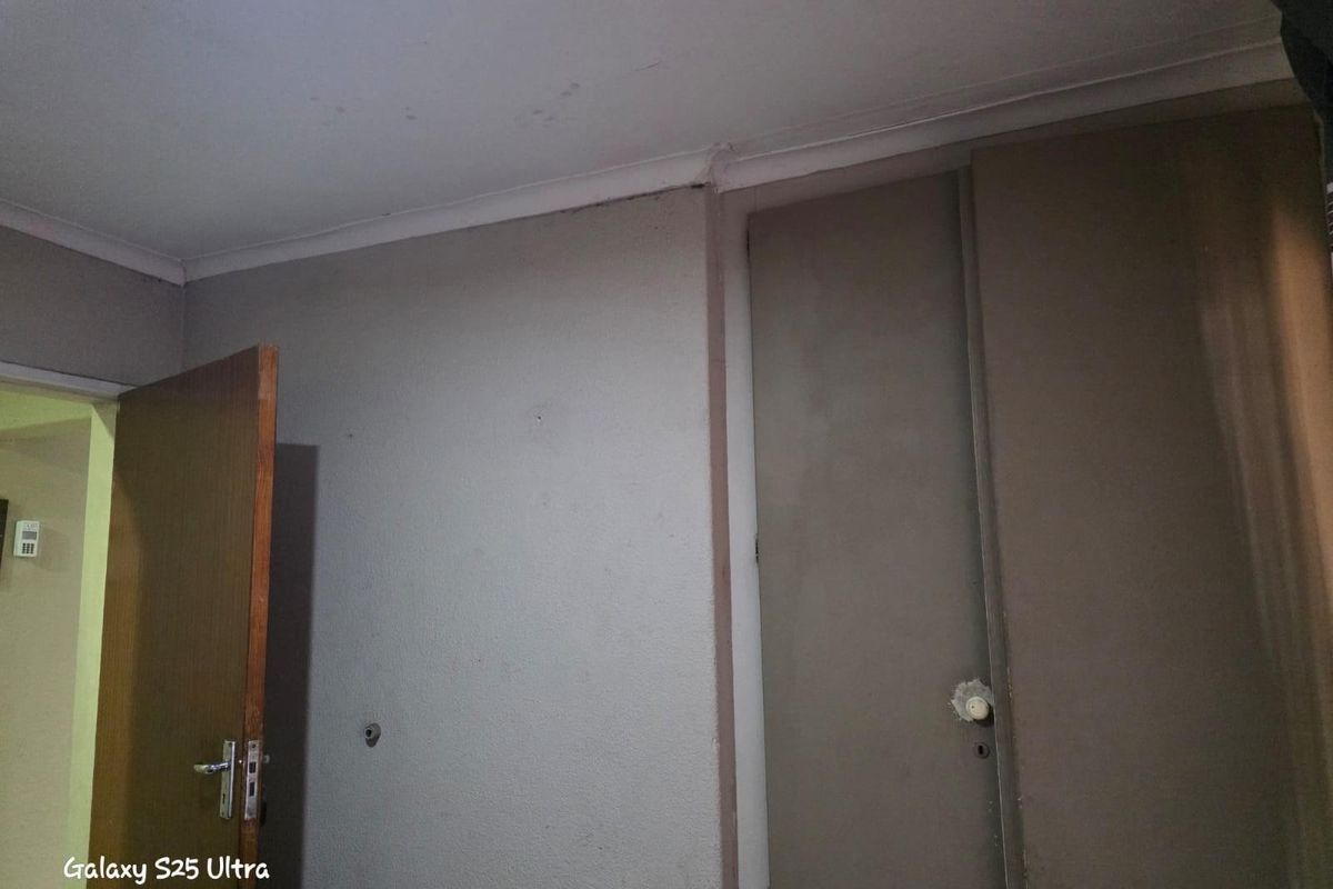 A bedroom interior featuring built-in cupboards, a standard door, and visible wear on the wall and ceiling finishes.