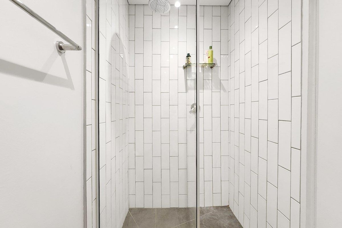 A modern walk-in shower featuring white subway wall tiles, a rainfall showerhead, a glass enclosure, and a grey tiled floor.