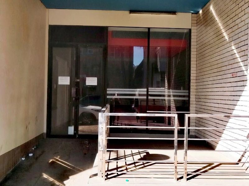 Commercial entrance featuring a glass door, brick facade, and stainless steel railing under a blue painted overhang.