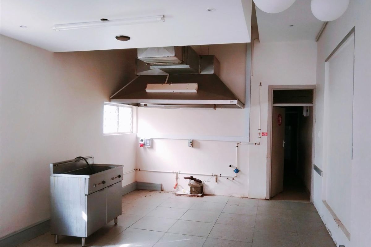 Commercial kitchen space featuring a stainless steel sink, industrial extractor hood, tiled flooring, and exposed utility connections.