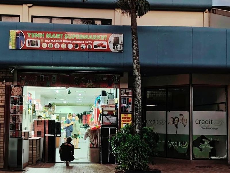 Commercial storefront featuring a supermarket entrance and adjacent office space with large glass windows and prominent signage on a paved street frontage.
