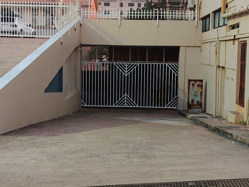 Exterior view of a commercial property featuring a gated basement parking entrance with a concrete driveway and external wall-mounted utility fixtures.