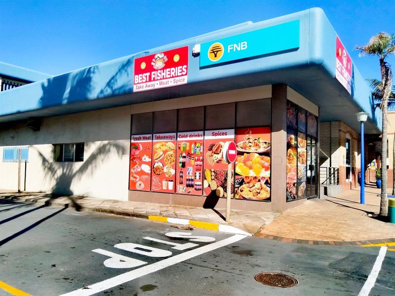 Commercial street-level retail storefront featuring large display windows with branding and signage, situated on a corner lot with paved access.