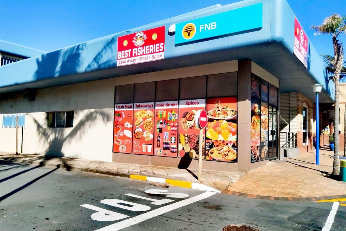 Commercial street-level retail storefront featuring large display windows with branding and signage, situated on a corner lot with paved access.