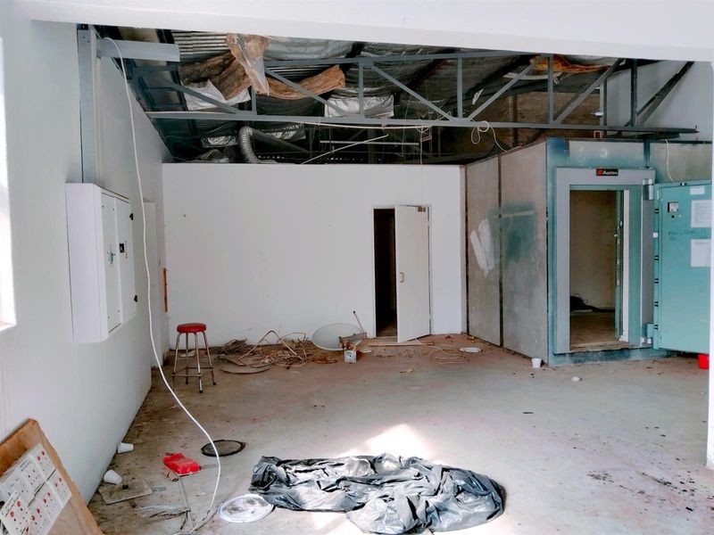An unfinished commercial utility space featuring exposed ceiling trusses, insulation, and a built-in walk-in cold storage unit.