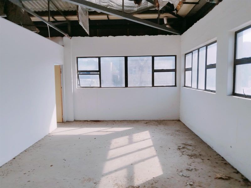 An empty commercial interior space featuring exposed ceiling rafters, large windows, and unfinished flooring, requiring significant renovation and finishing work.