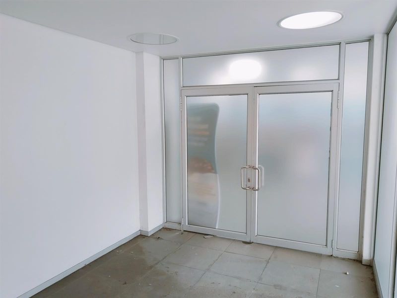 A clean, minimalist commercial entry area featuring frosted glass double doors, recessed ceiling lighting, and neutral tiled flooring.