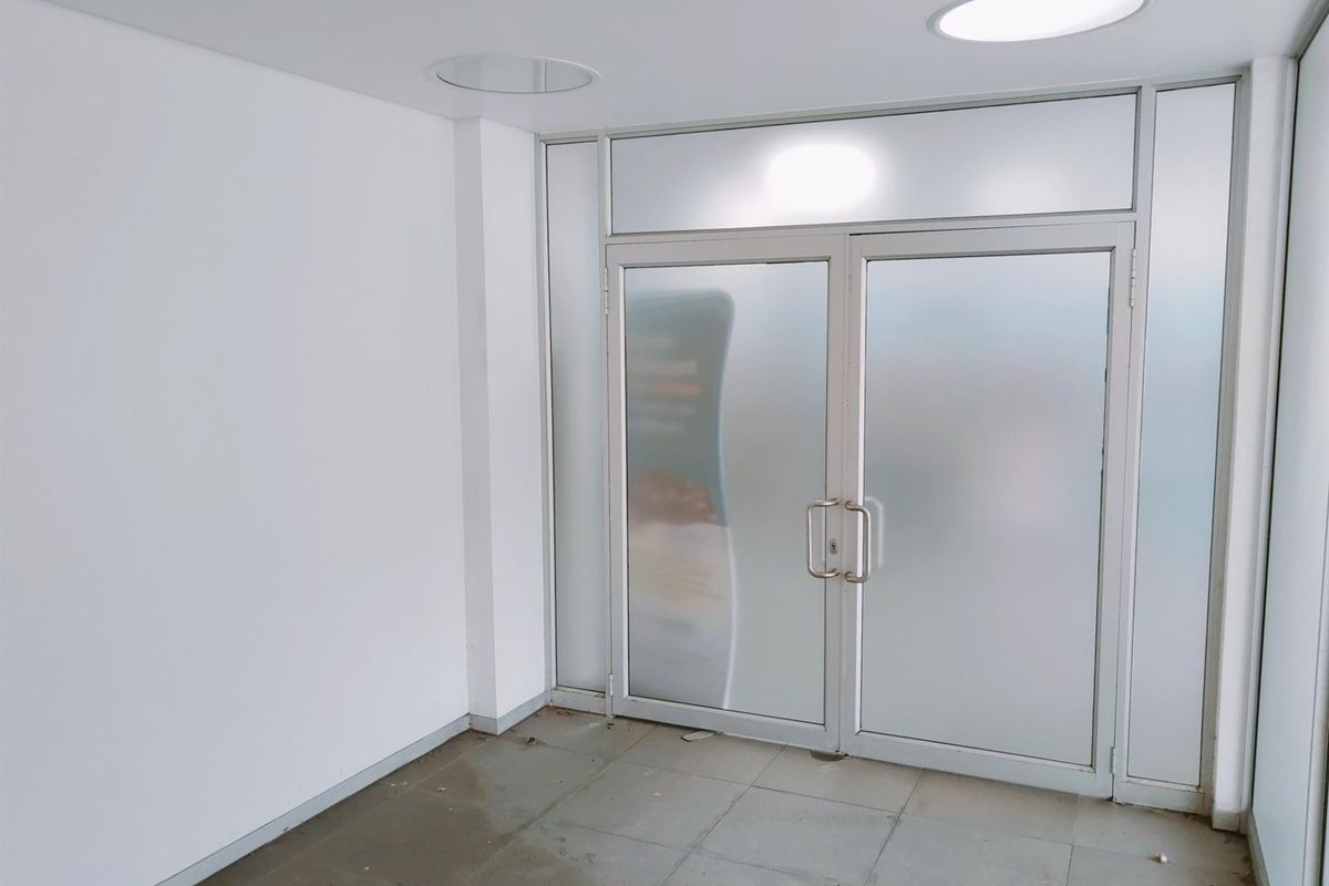 A clean, minimalist commercial entry area featuring frosted glass double doors, recessed ceiling lighting, and neutral tiled flooring.