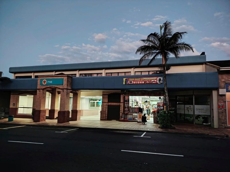 Commercial retail strip featuring a bank branch and supermarket with paved frontage and prominent signage along a main access road.