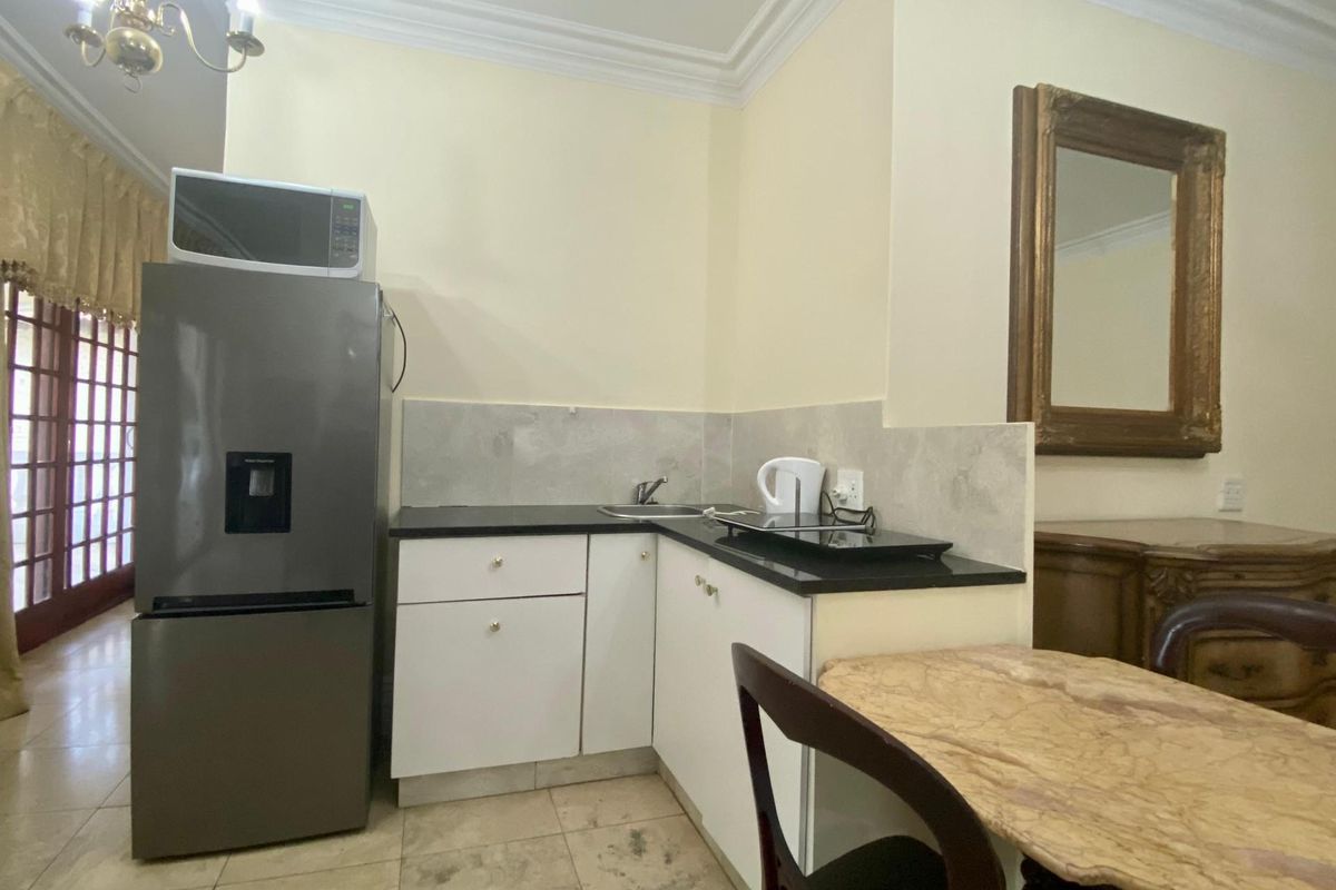 Compact kitchenette featuring white cabinetry, black countertops, a stainless steel sink, and tiled flooring, suitable for a small apartment or studio space.