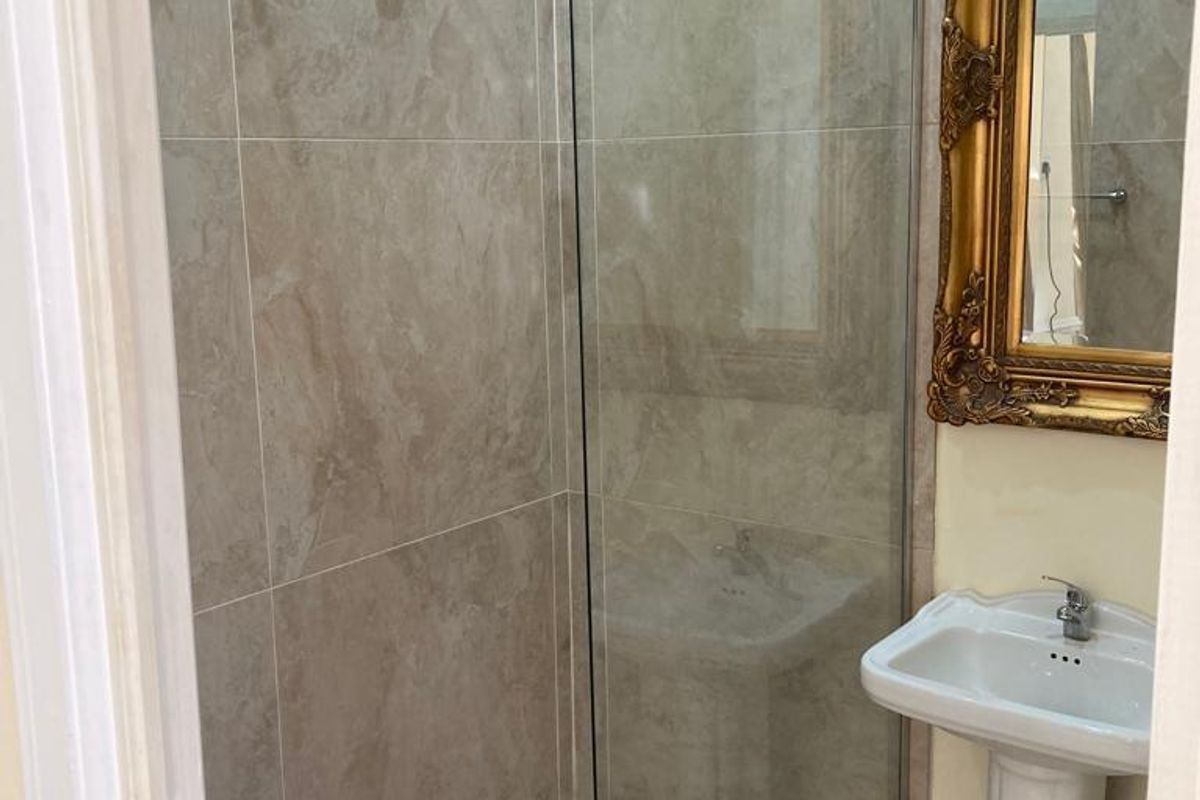 A modern bathroom featuring a glass-enclosed walk-in shower with neutral wall tiling and a classic pedestal sink.