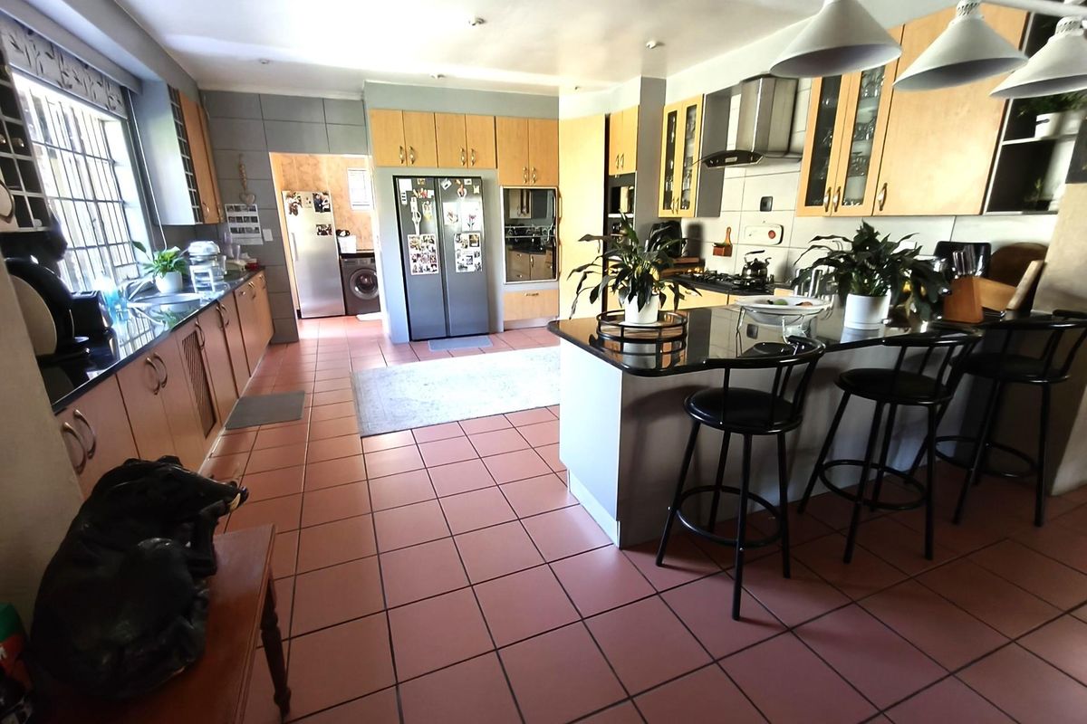 Spacious kitchen featuring light wood cabinetry, granite countertops, a central island with breakfast bar seating, and an adjoining scullery area.