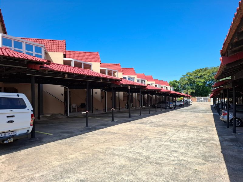 A row of apartment units featuring covered parking bays with red tiled roofs and concrete driveway access.