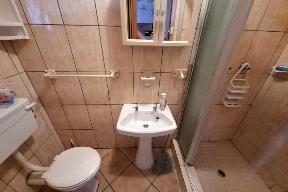 A compact bathroom featuring a pedestal sink, a toilet, and a glass-enclosed shower stall with neutral wall and floor tiling.